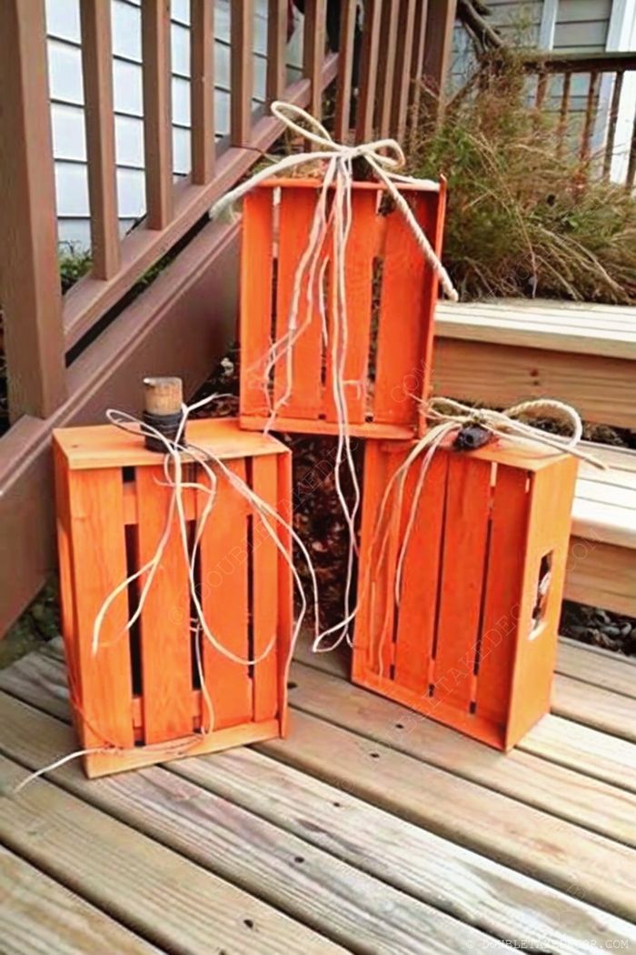 Three painted orange wooden crates with rustic twine accents arranged on a deck, topped with decorative elements for seasonal fall decor.