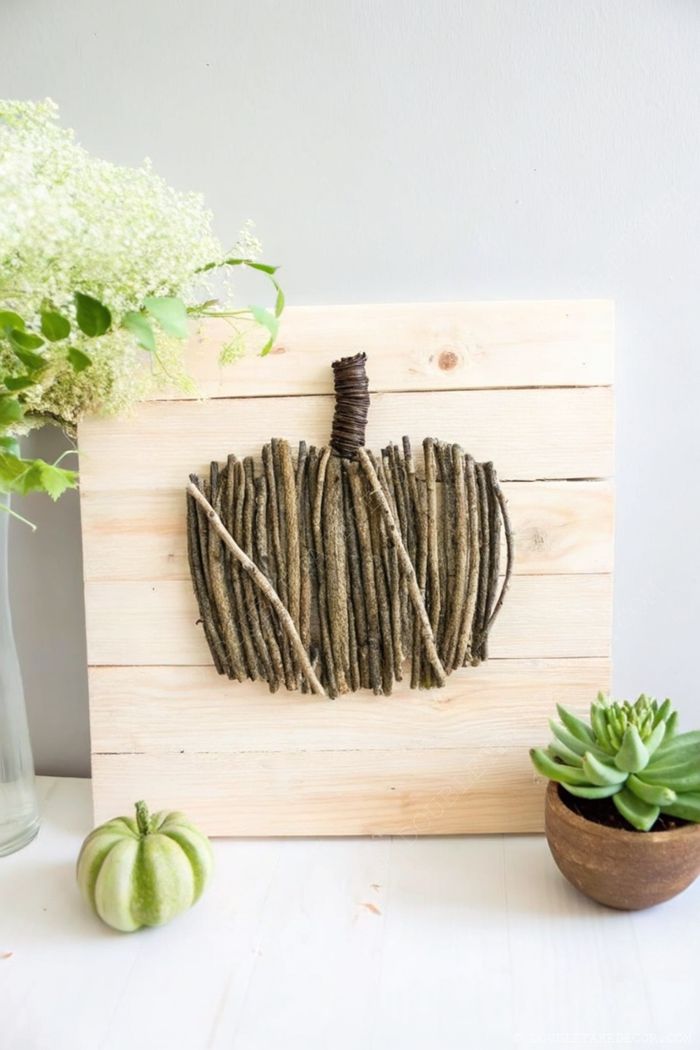 Charming twig pumpkin centerpiece with white flowers and succulent, arranged on wooden planks for fall decor.