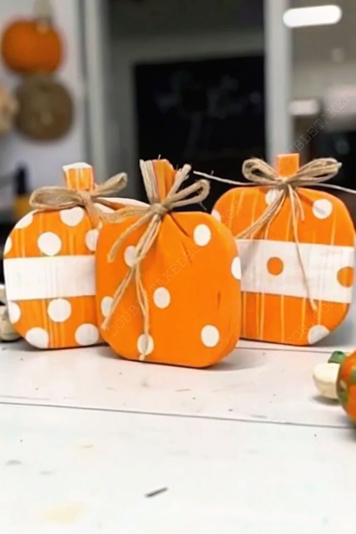 Decorative wooden pumpkins painted in bright orange with polka dots and stripes, topped with stems and rustic twine for autumn home decor.