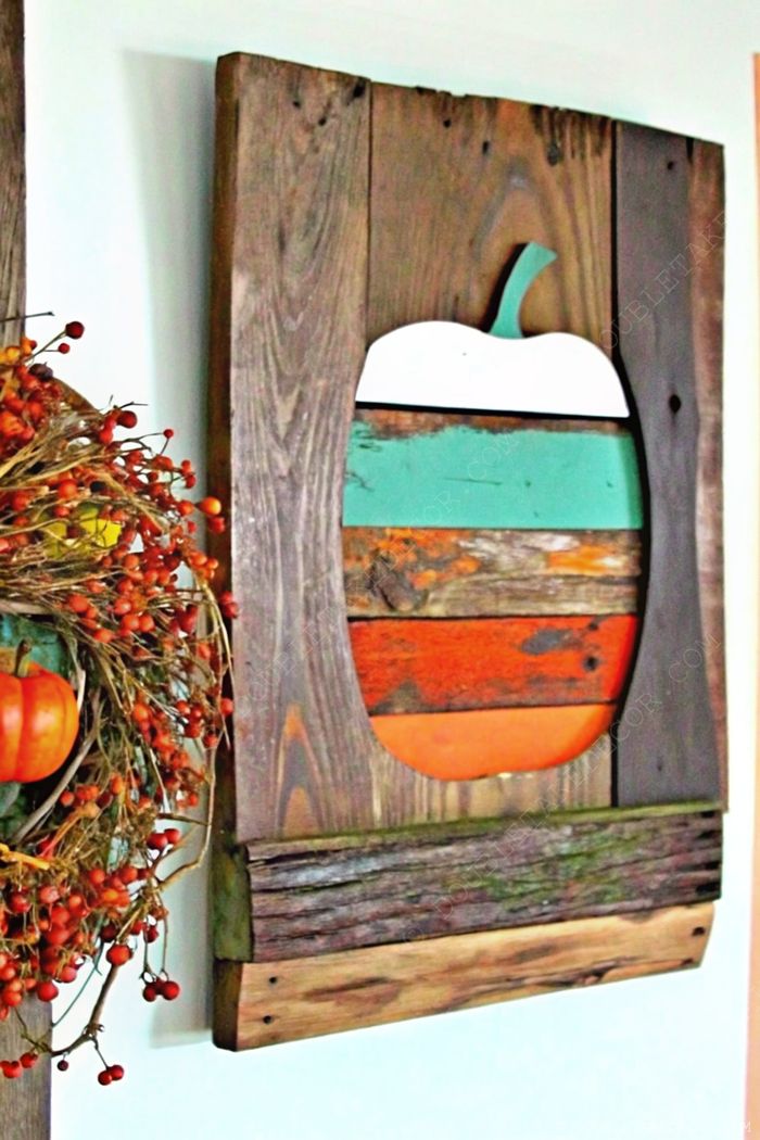 Rustic wall decor featuring an apple design made from teal, orange, and brown wood planks, complemented by a natural twig wreath with red berries for fall decor.