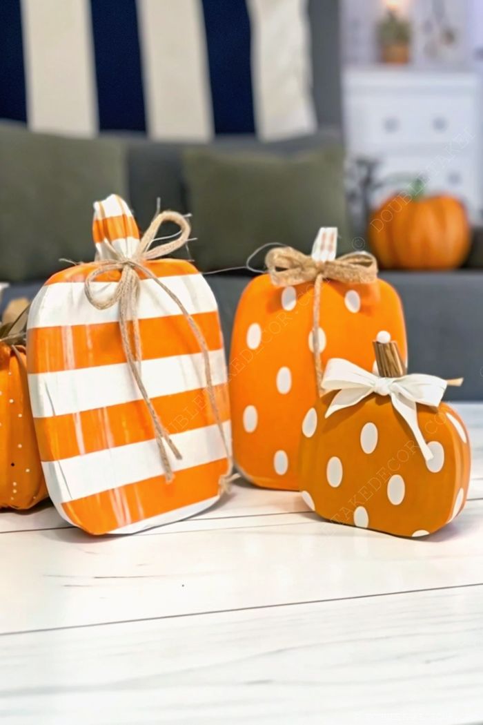 Three decorative pumpkins on a wooden surface: one with orange and white stripes, two with white polka dots, all with burlap bows.