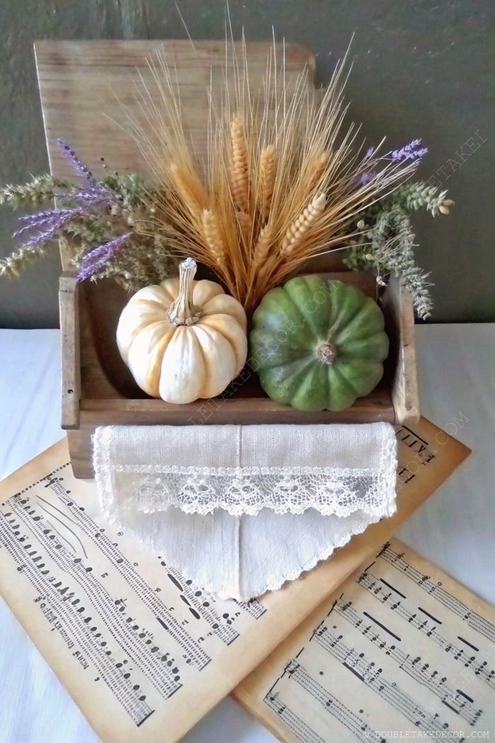 Rustic wooden box with creamy white and green decorative pumpkins, dried wheat and lavender, lace trim, and vintage sheet music backdrop.