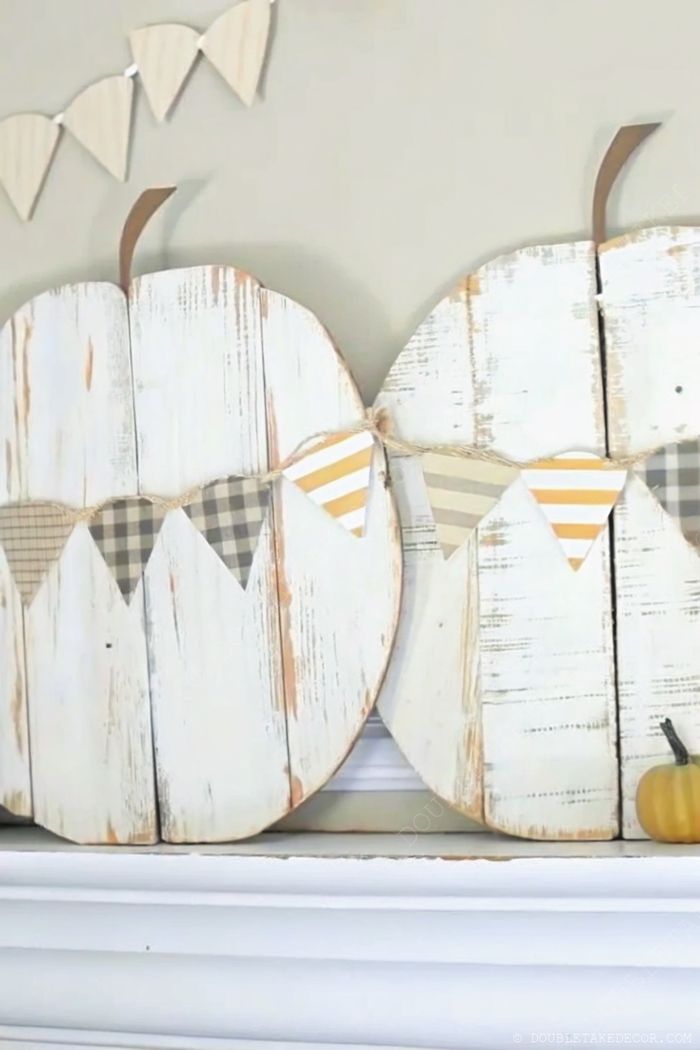 Autumn decor with distressed white wooden pumpkins, earthy patterned bunting, and small orange pumpkin creating a cozy fall arrangement