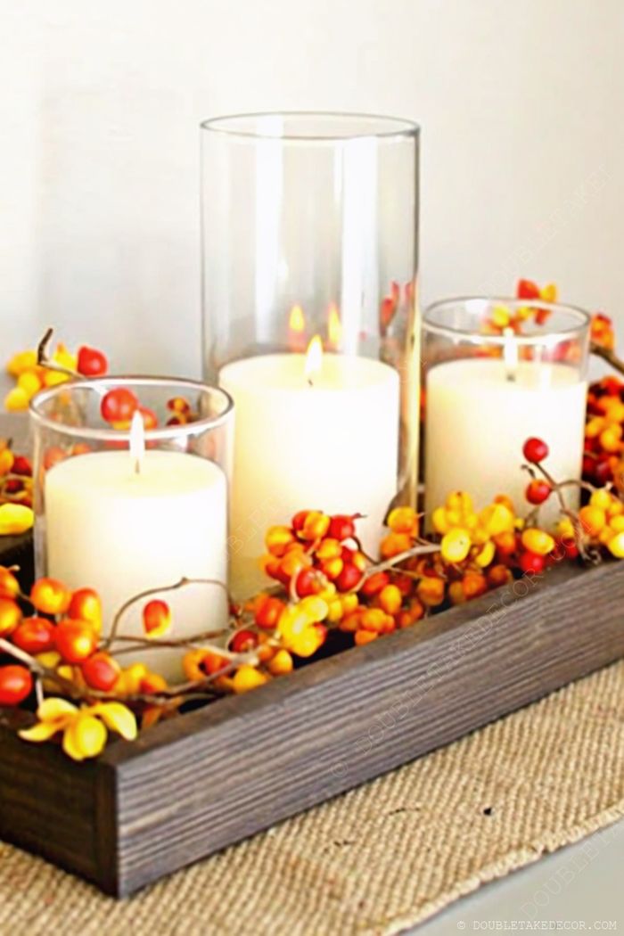 White candles arranged on a wooden tray with colorful autumn berries, creating a cozy fall centerpiece on burlap runner