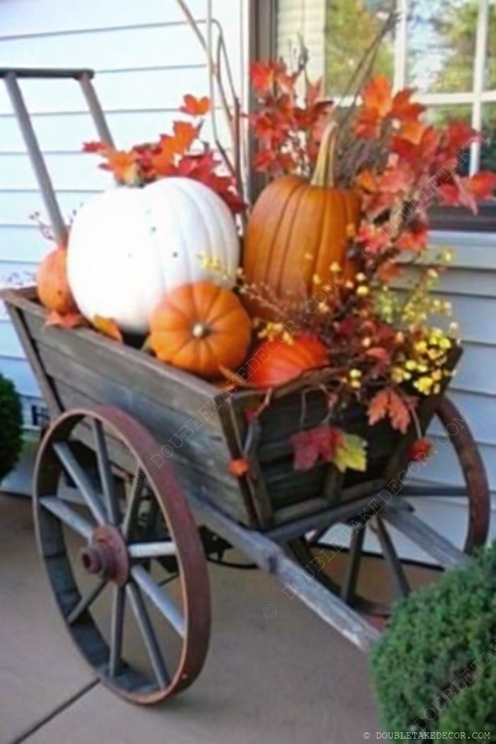 Weathered wooden wheelbarrow filled with assorted pumpkins, fall leaves, and flowers creating a charming outdoor fall decoration.