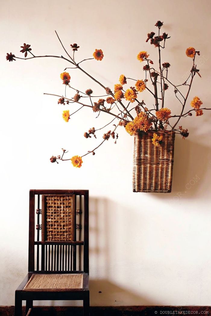 Dark wooden chair beside wall-mounted woven basket with yellow blossoming branches, creating a warm natural decor aesthetic.