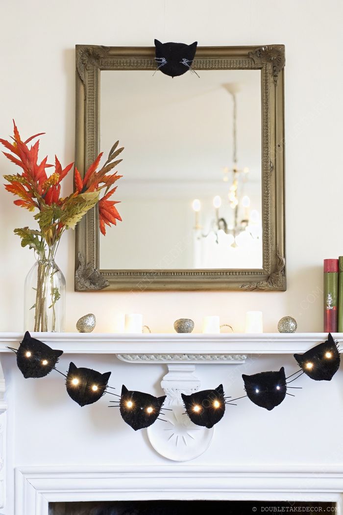 Elegant fireplace mantel adorned with cat-shaped string lights, autumn foliage in a vase, and decorative accents, creating a festive Halloween ambiance.