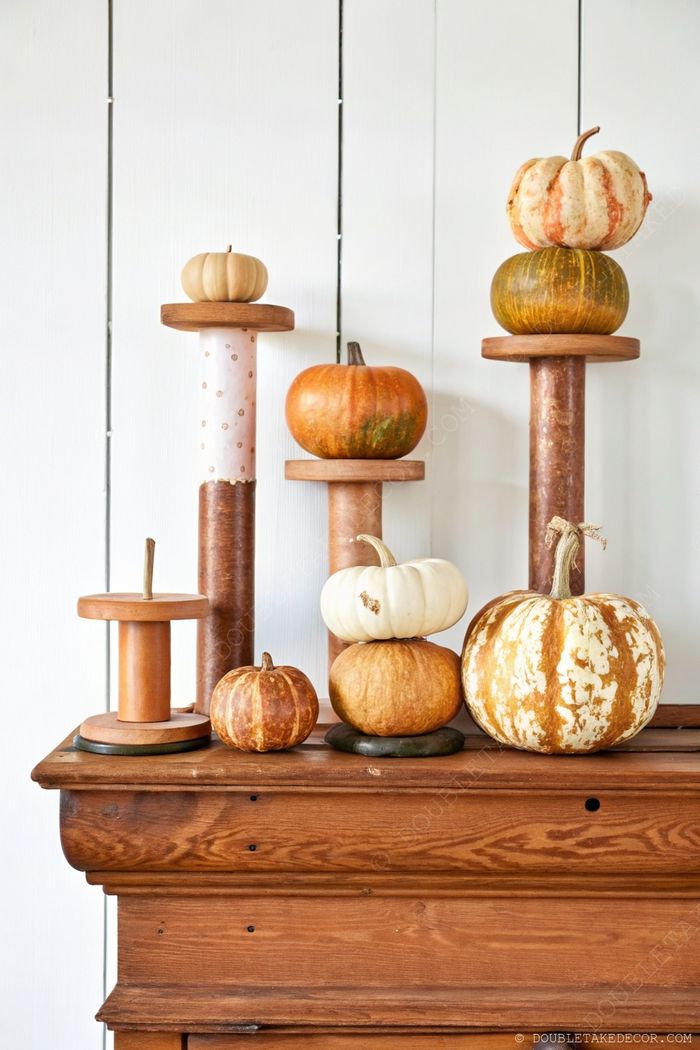Autumn display of decorative pumpkins arranged on wooden pedestals with orange, white, and green colors against wooden panels.