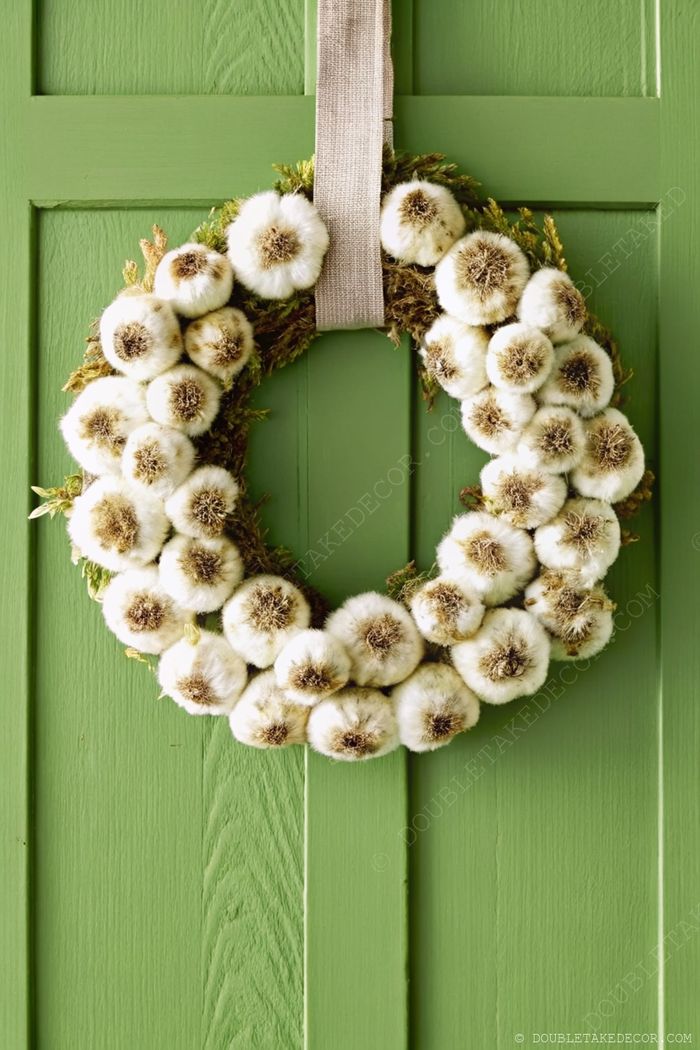 Rustic wreath with white fluffy pom-poms resembling cotton bolls arranged on a moss base hanging on a bright green door.