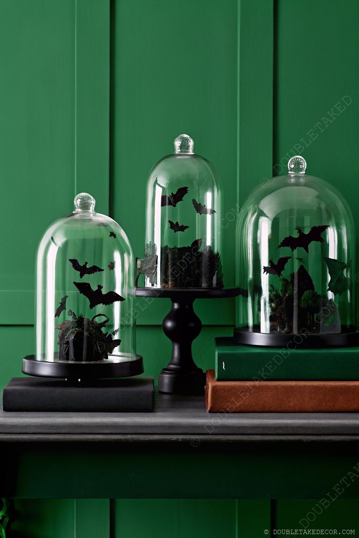 Halloween glass cloches with black bat silhouettes and dark foliage displayed on pedestals with vintage books, creating sophisticated spooky decor.