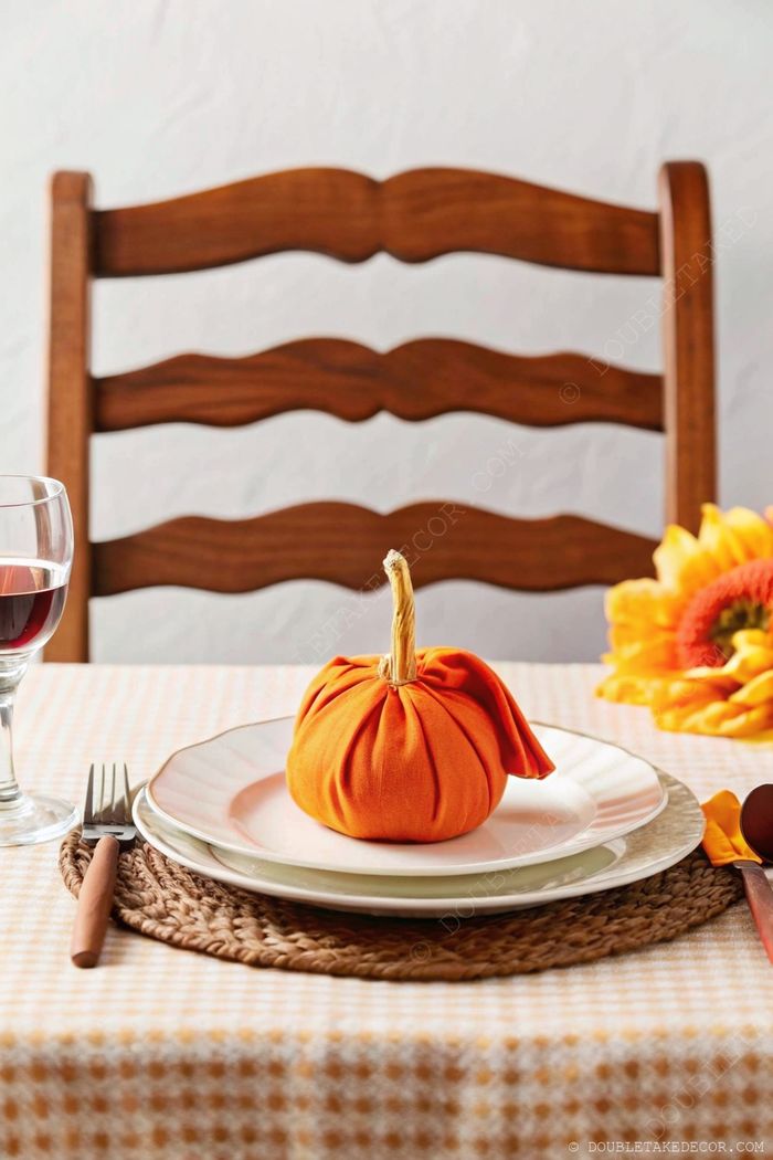 Warm autumn dining table with orange fabric pumpkin centerpiece, sunflowers, and wine glass on textured tablecloth