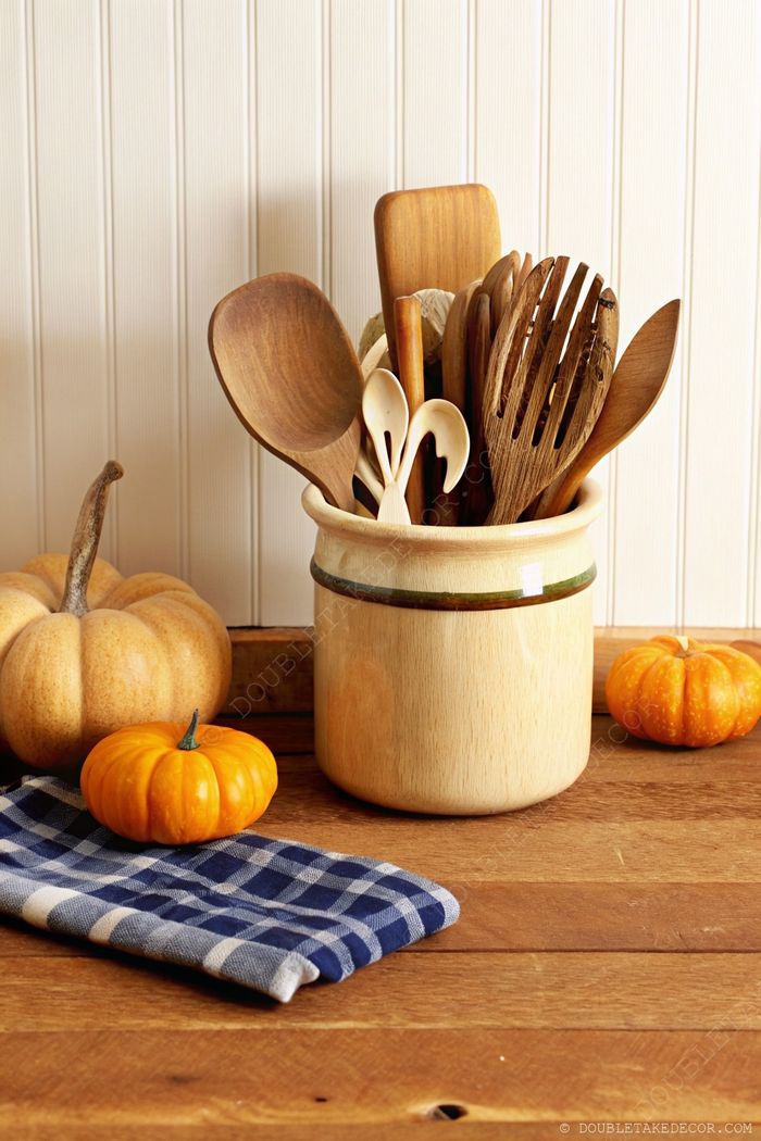 Kitchen utensil holder with wooden spoons, decorated with seasonal pumpkins on a blue checkered cloth for Halloween ambiance.