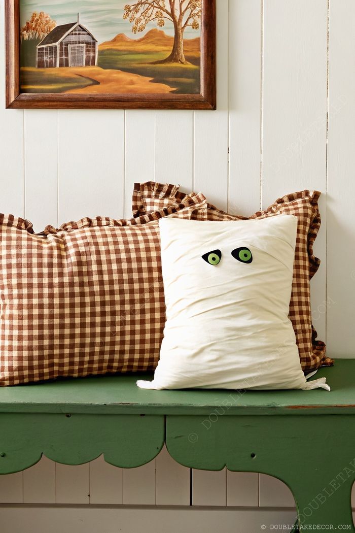 Rustic green bench with checkered pillow and whimsical mummy pillow, complemented by a framed landscape painting.