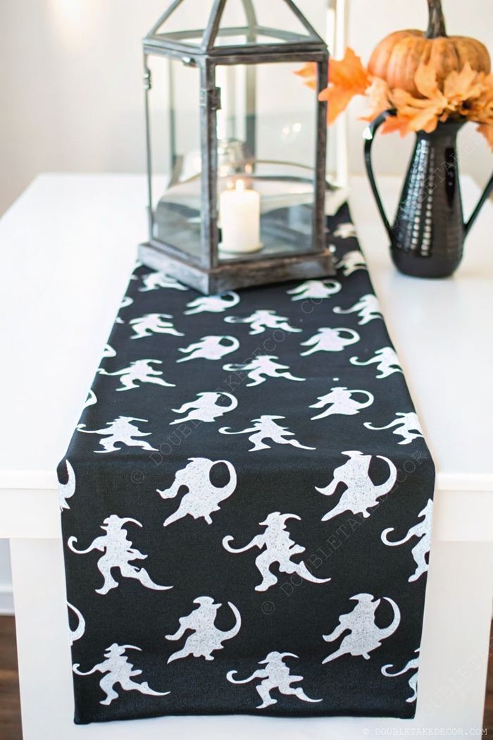 Elegant Halloween table runner with cat silhouettes, glass lantern, and seasonal decor of autumn leaves and pumpkin.