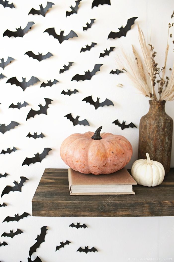 Charming fall display with pale pumpkins on stacked books, black bat decorations on wall, and pampas grass accents.