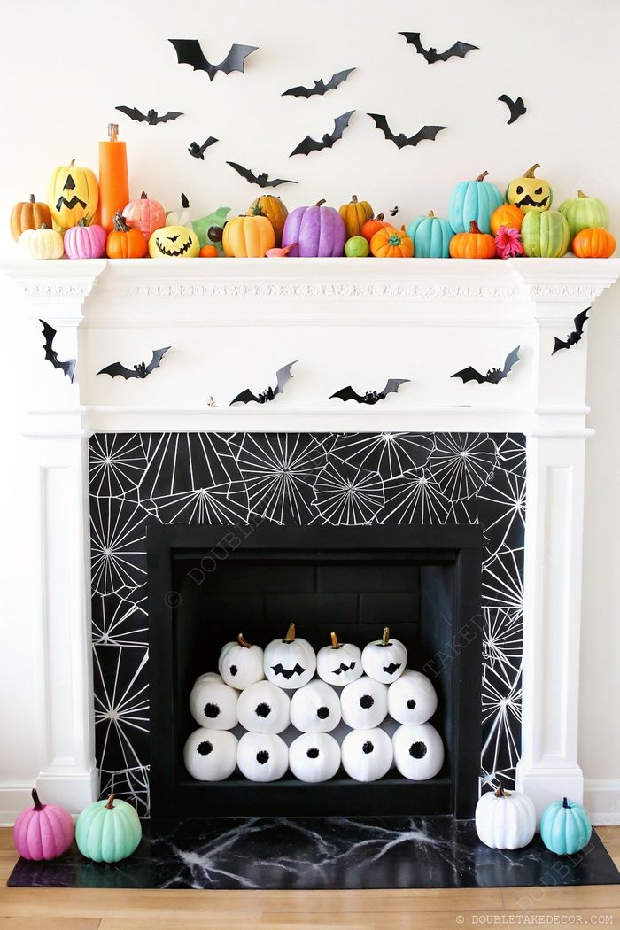 Halloween mantel adorned with colorful pumpkins, flying black bats, and a fireplace filled with white jack-o'-lanterns against a spiderweb backdrop.
